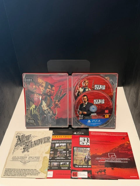 Red Dead Redemption II Ultimate Edition PS4 open SteelBook showing both discs, New Hanover map insert and Ultimate Edition bonus content insert