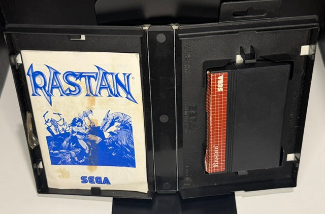 Rastan Sega Master System open case showing manual with yellowing and foxing stain and SMS cartridge with red Sega label