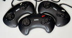 Four official Sega Mega Drive Control Pad 3-button wired controllers in black showing varying cosmetic wear consistent with Grade B pre-owned condition